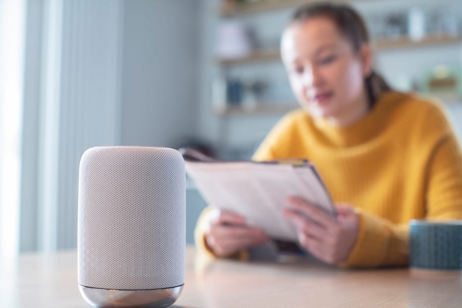 Femme lisant un magazine à la maison posant une question à l'assistant numérique